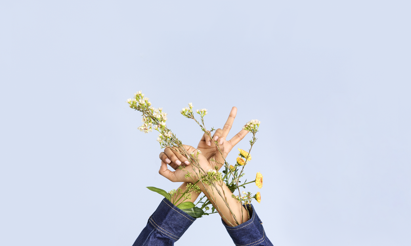 Two hands with flowers entwined among the fingers, set against a plain blue background.